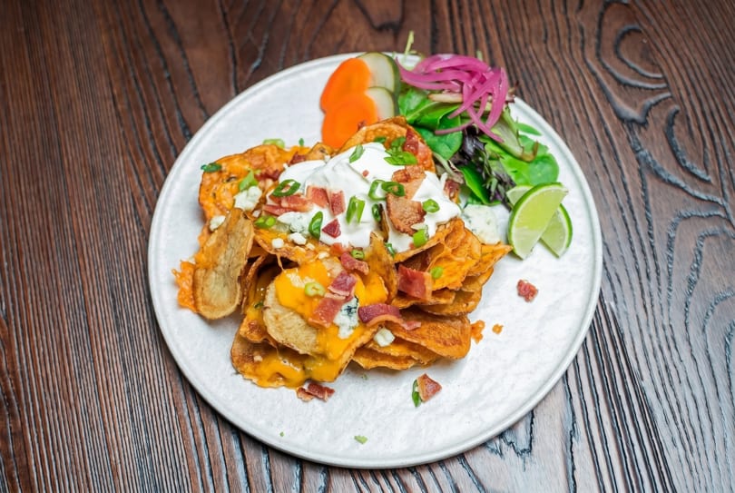 Loaded potato chips with melted cheese, bacon, sour cream, chives, and a side salad.