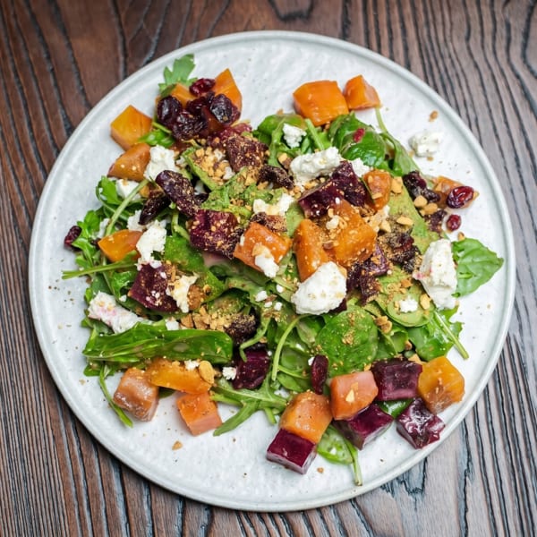 Colorful salad with mixed greens, roasted beets, butternut squash, goat cheese, and nuts on a white plate.
