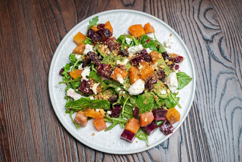 Colorful salad with mixed greens, roasted beets, butternut squash, goat cheese, and nuts on a white plate.