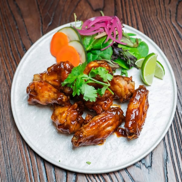 Glazed chicken wings with cilantro, pickled onions, carrots, cucumbers, and lime on a white plate.