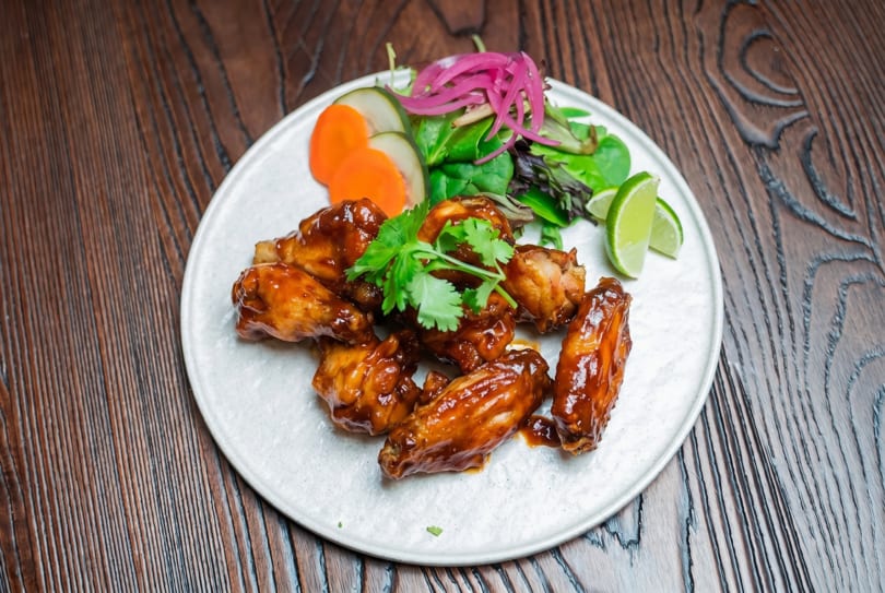 Glazed chicken wings with cilantro, pickled onions, carrots, cucumbers, and lime on a white plate.