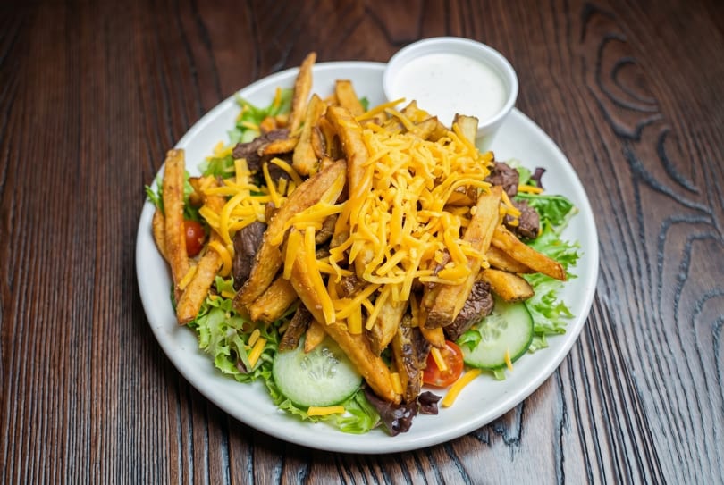 Steak salad with french fries, shredded cheddar cheese, and a side of ranch dressing.