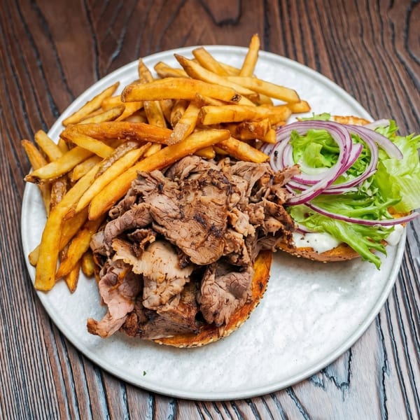 Open-faced beef sandwich with lettuce, red onion, and fries on a white plate.