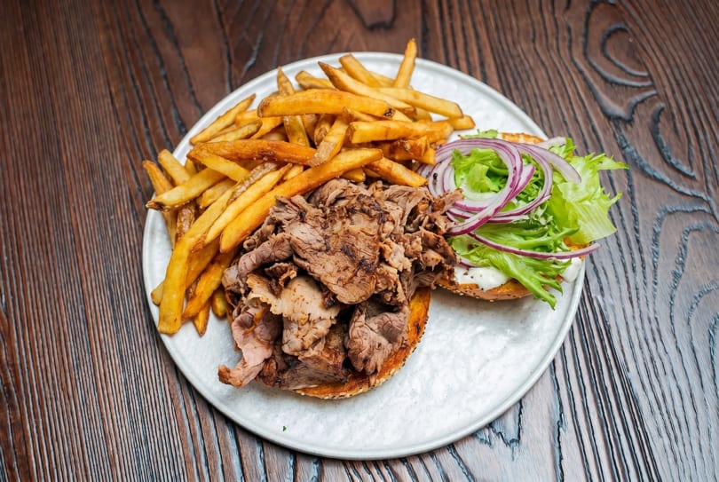 Open-faced beef sandwich with lettuce, red onion, and fries on a white plate.